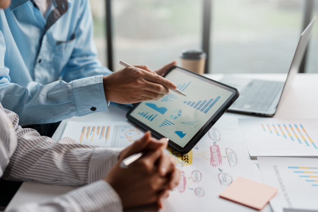 Business team together to make investment planning on digital tablet at the meeting. Close-up of a business consultant pointing to graphs and charts analyzing company growth to expand the product line.